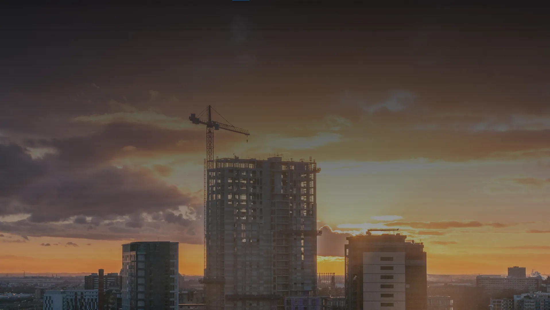 A high-rise under construction at sunset with a tower crane in silhouette